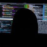 Person in silhouette in front of screens showing code